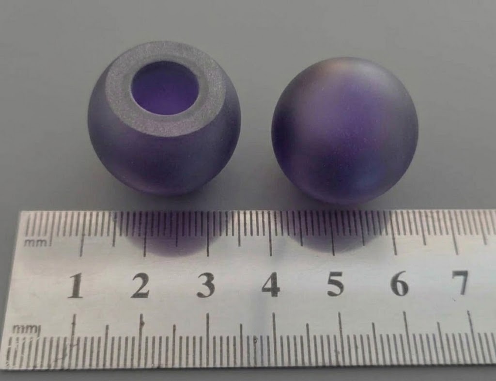 Two frosted purple spherical parts, one with a through hole, next to a ruler