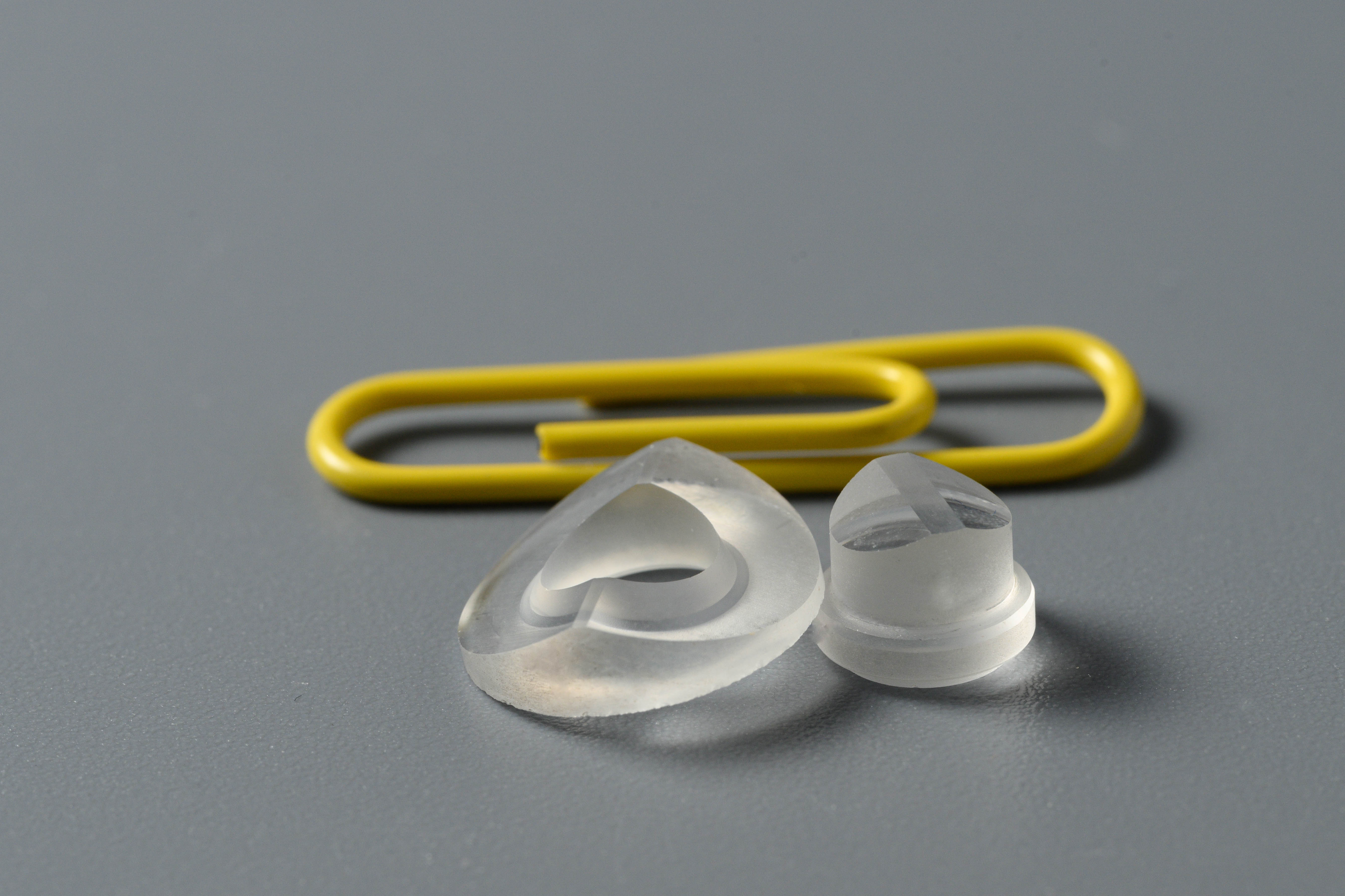 Small frosted prism and dome-shaped optical parts next to a paperclip