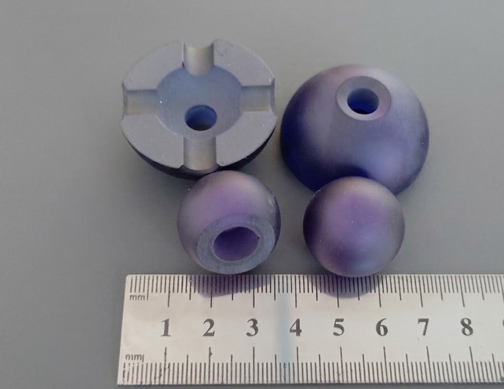 Frosted spherical and hemispherical blanks with center bores, shown with a holder fixture and ruler