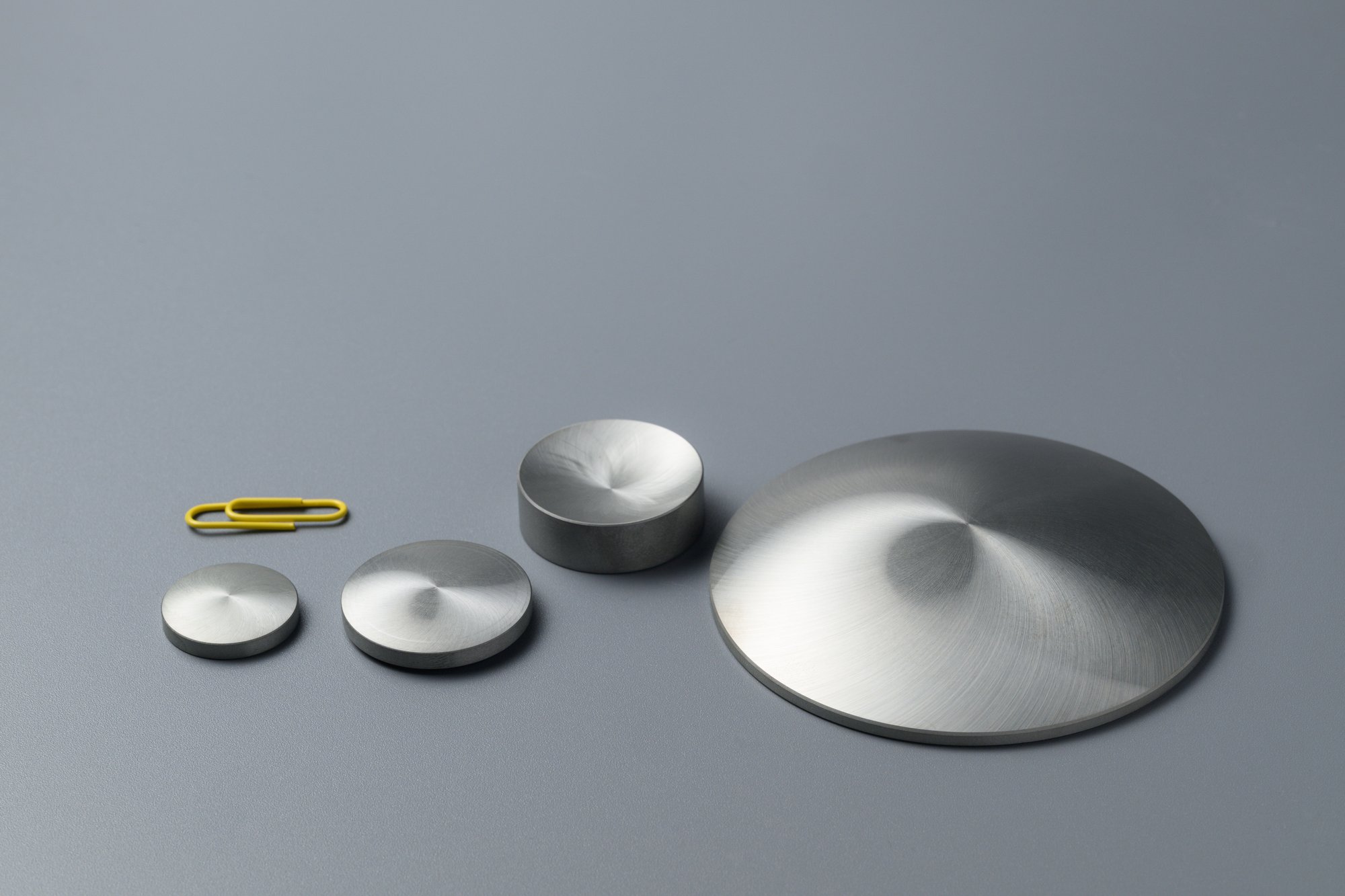 Metal optical elements with conical and concave surfaces next to a paper clip
